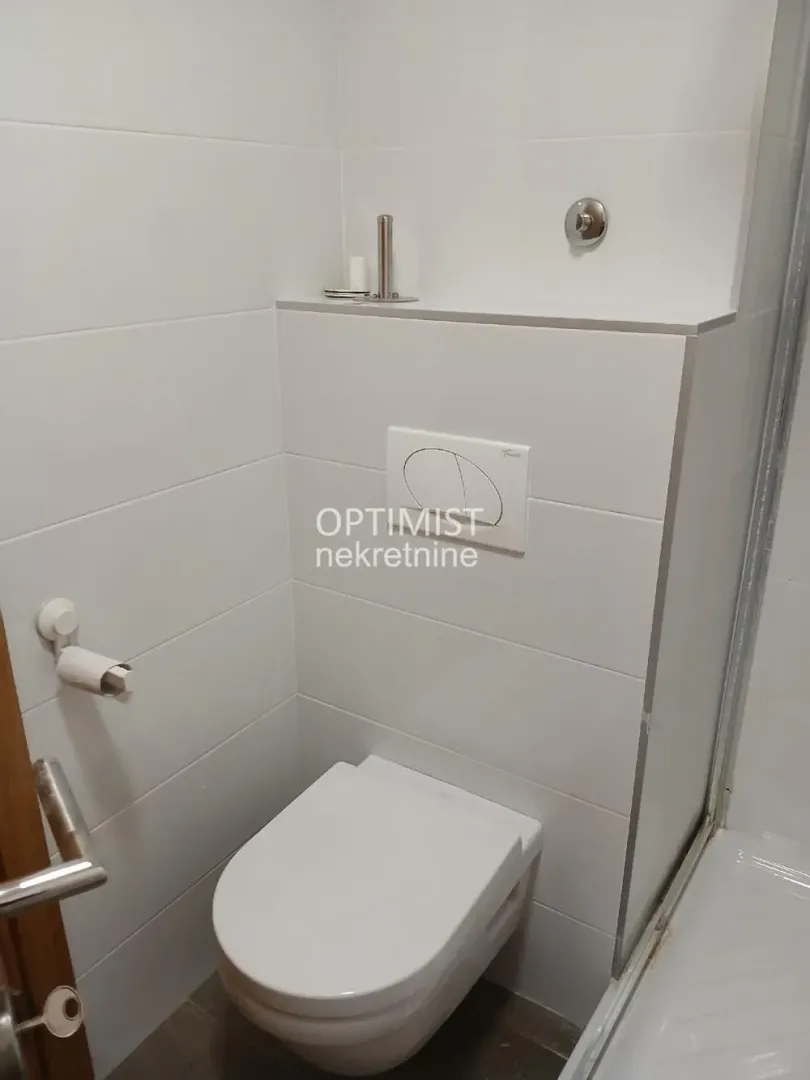 Moderno opremljeno kupatilo sa WC šoljom i belim pločicama.