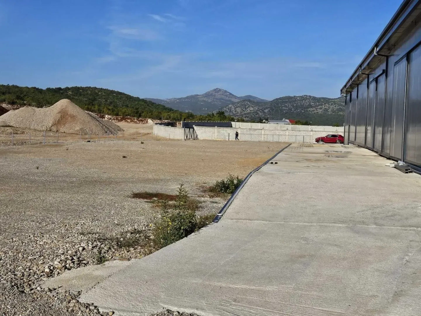 Spacious outdoor yard with a concrete driveway in front of an industrial building.