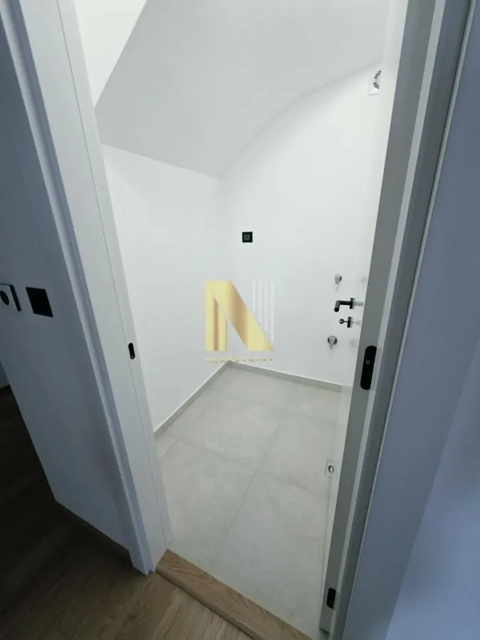 Pogled kroz vrata na moderno opremljeno kupatilo sa belim pločicama.