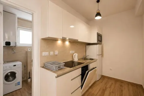 Modern kitchen with white cabinetry and a view into the bathroom with a washing machine. - image 5