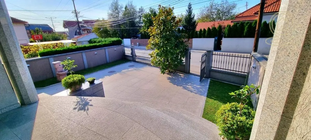 Paved courtyard with a gate and landscaped greenery in front of the house.