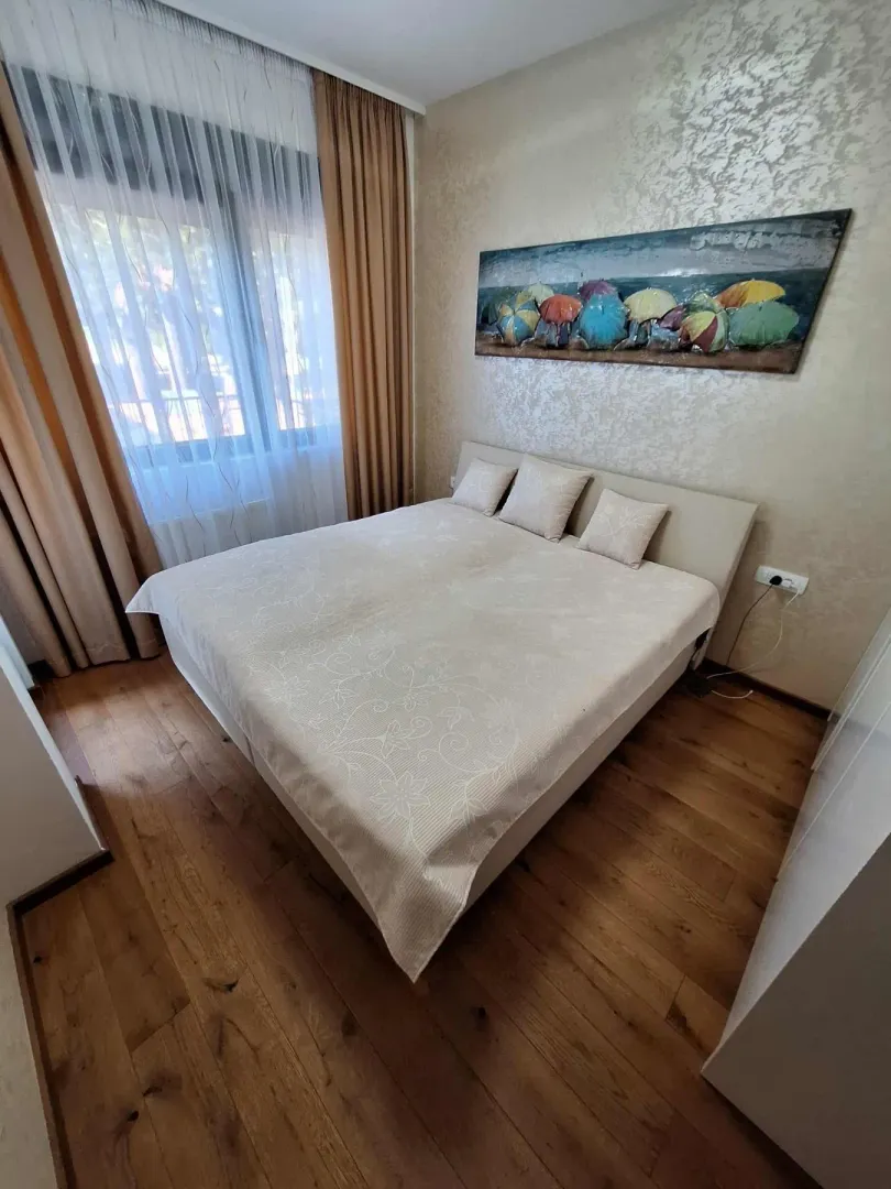 Namještena spavaća soba sa bračnim krevetom, drvenim podom i prozorom sa zavjesama.