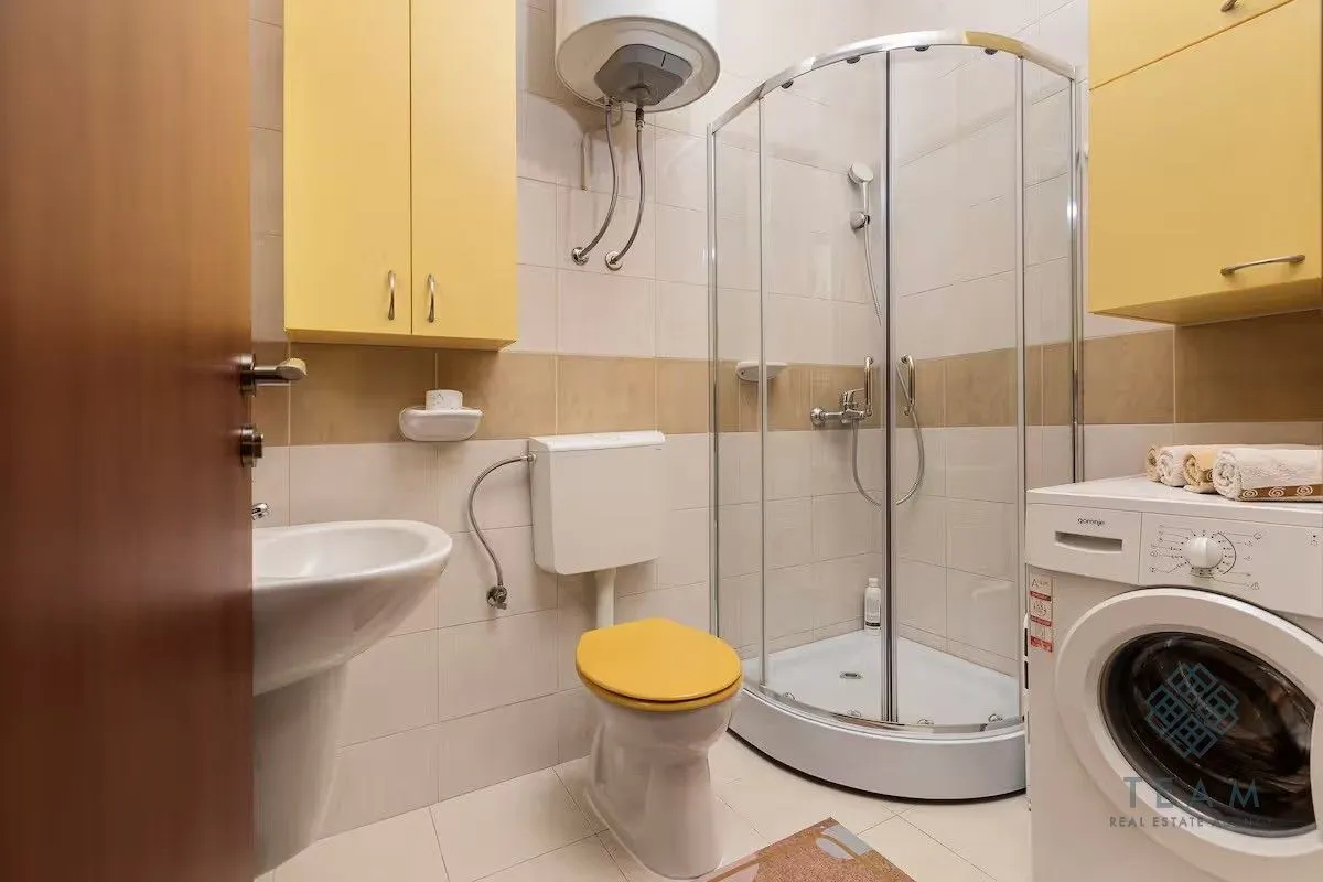 Bathroom with a shower cabin, washbasin, toilet bowl, and washing machine.