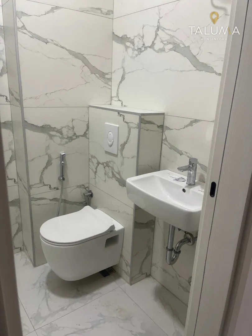 Small bathroom with white marble-pattern tiles, a wall-hung toilet, and a washbasin.