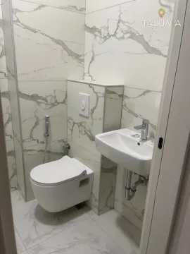 Small bathroom with white marble-pattern tiles, a wall-hung toilet, and a washbasin. - image 3