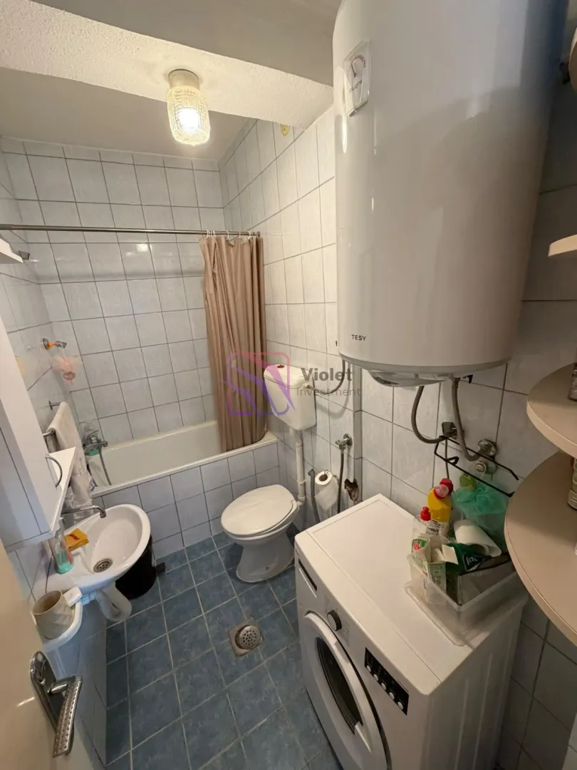 Manje kupatilo opremljeno kadom, toaletom, umivaonikom i mašinom za veš.