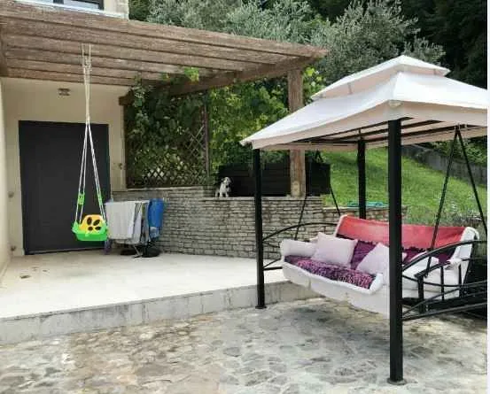 Popločano dvorište ispred kuće sa natkrivenom ljuljaškom i dječjom ljuljaškom.