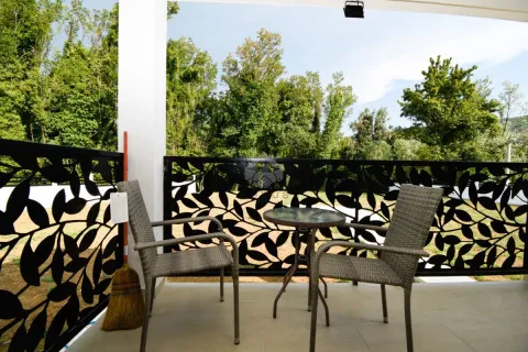 Covered terrace with a table, two chairs, and a view of greenery. - image 14