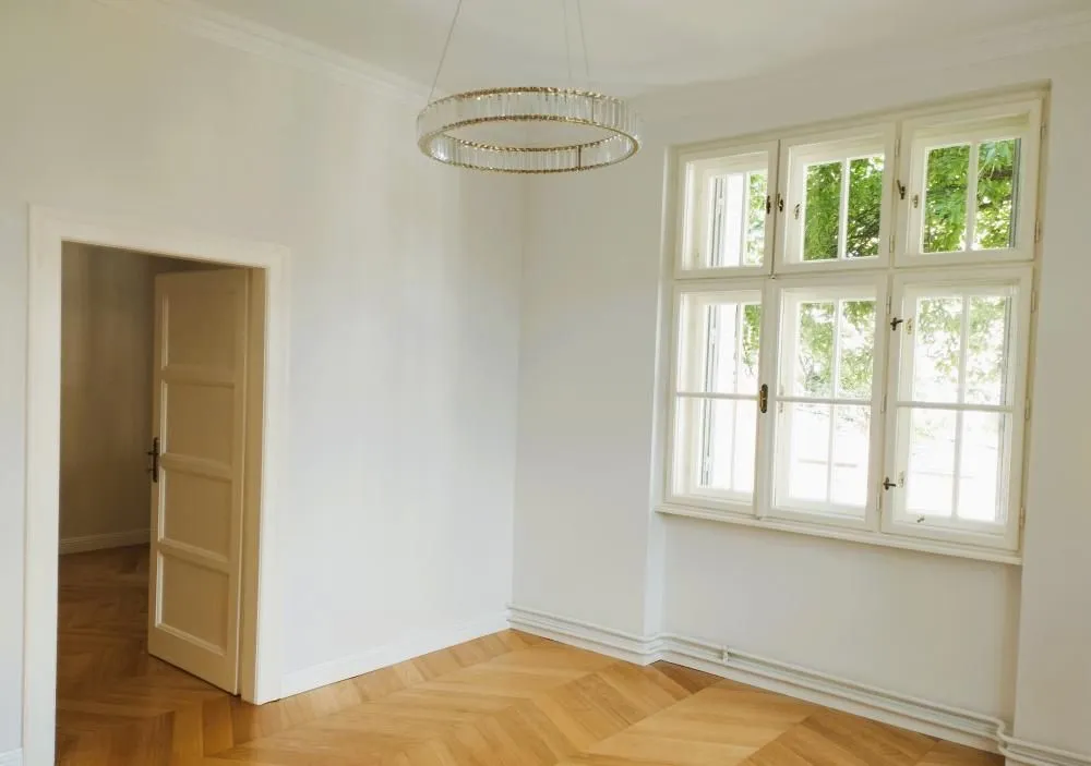 Empty bright room with parquet flooring and a large window.