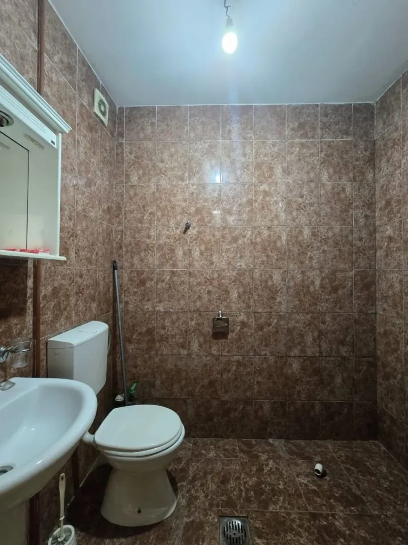 Manje kupatilo obloženo smeđim keramičkim pločicama sa osnovnim sanitarijama.