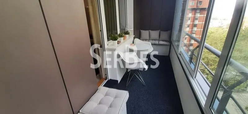 Zastakljeni balkon sa garniturom za sedenje i malim stolom.