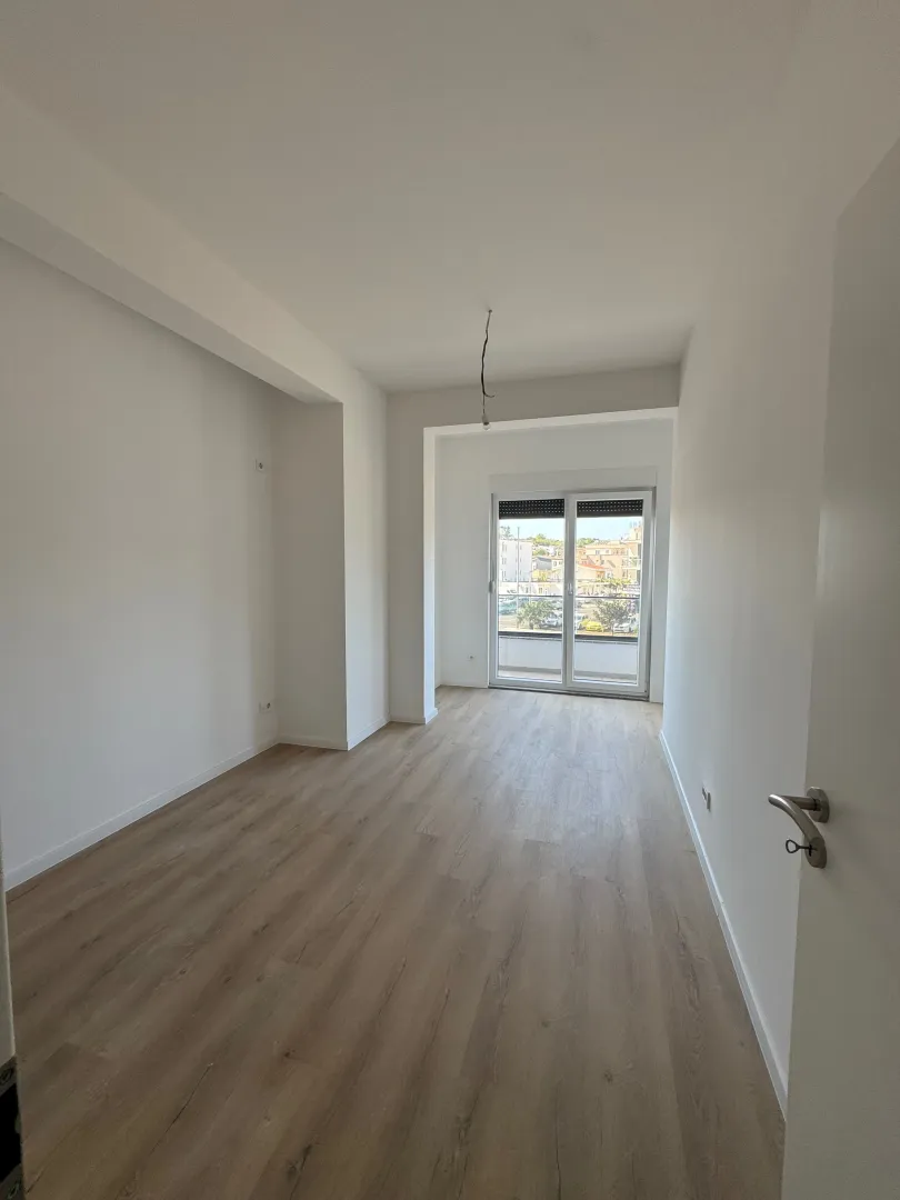Prazna soba sa laminatom i izlazom na balkon.