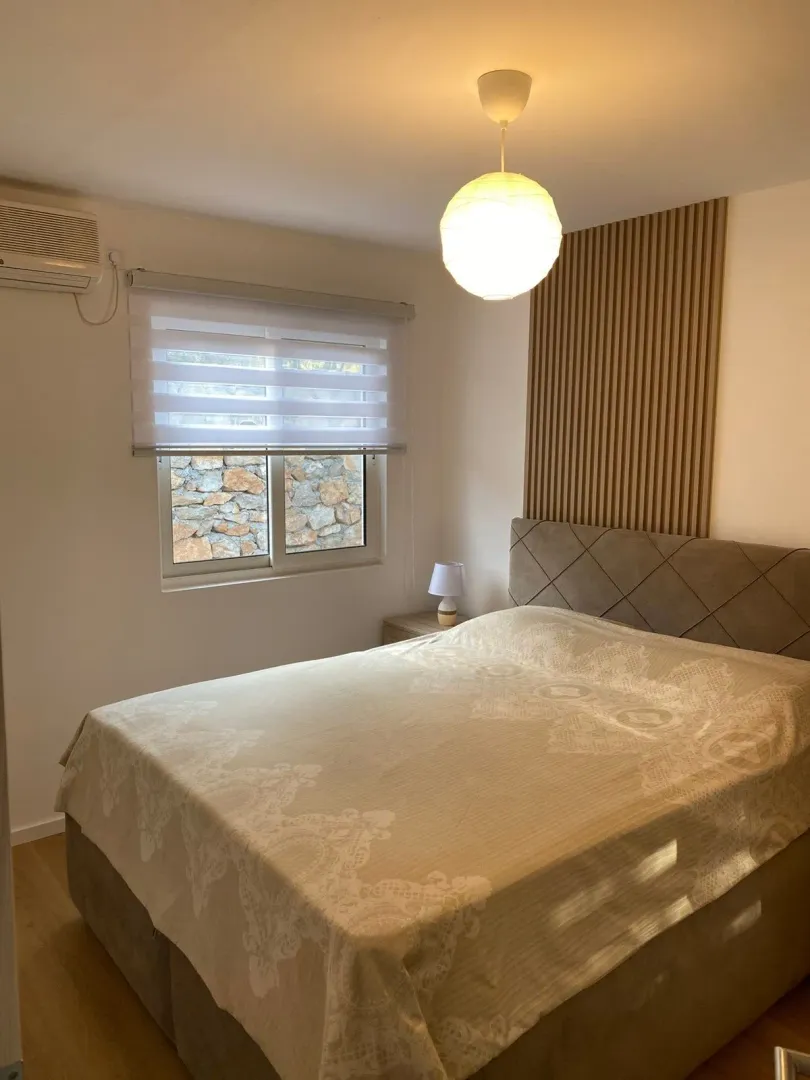 Furnished bedroom with a double bed, window, and decorative wall panel.