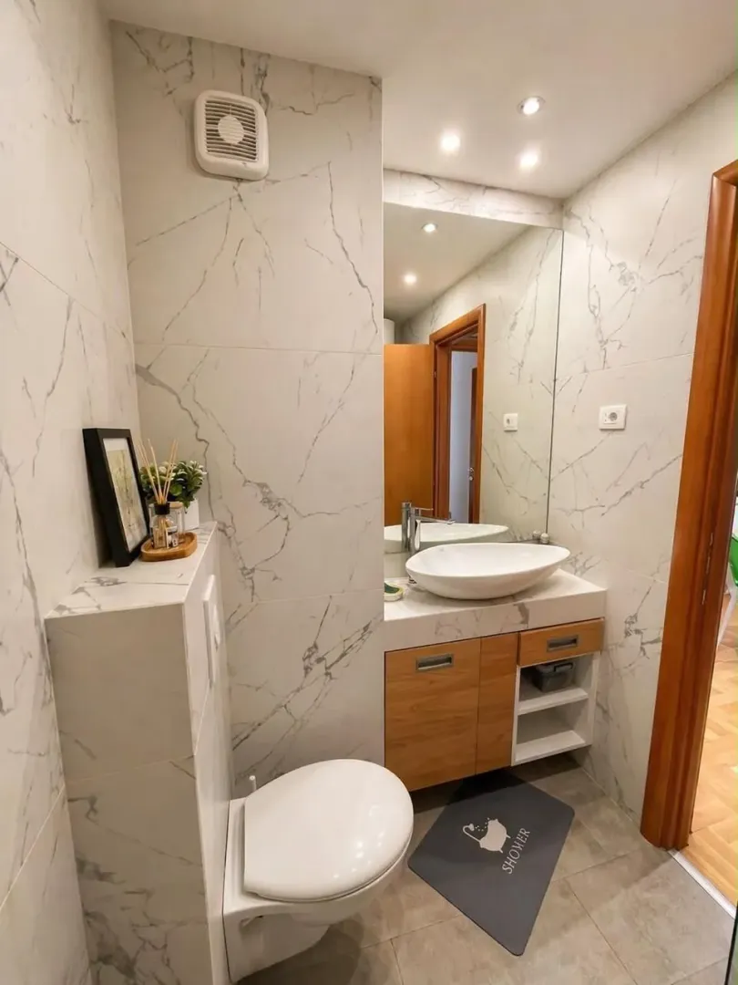 Modern bathroom with washbasin, toilet, and marble tiles.