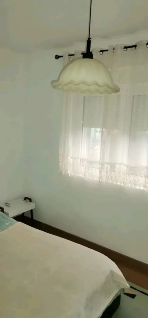 A simple bedroom featuring a window and a hanging light.