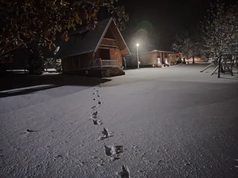Noćni snimak drvene kuće i dvorišta prekrivenog snegom sa tragovima stopala. - image 16