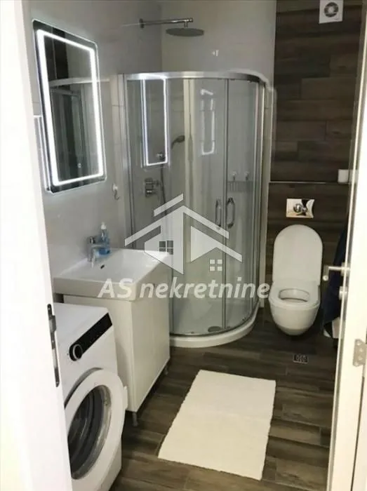 Savremeno opremljeno kupatilo sa tuš kabinom, umivaonikom i veš mašinom.
