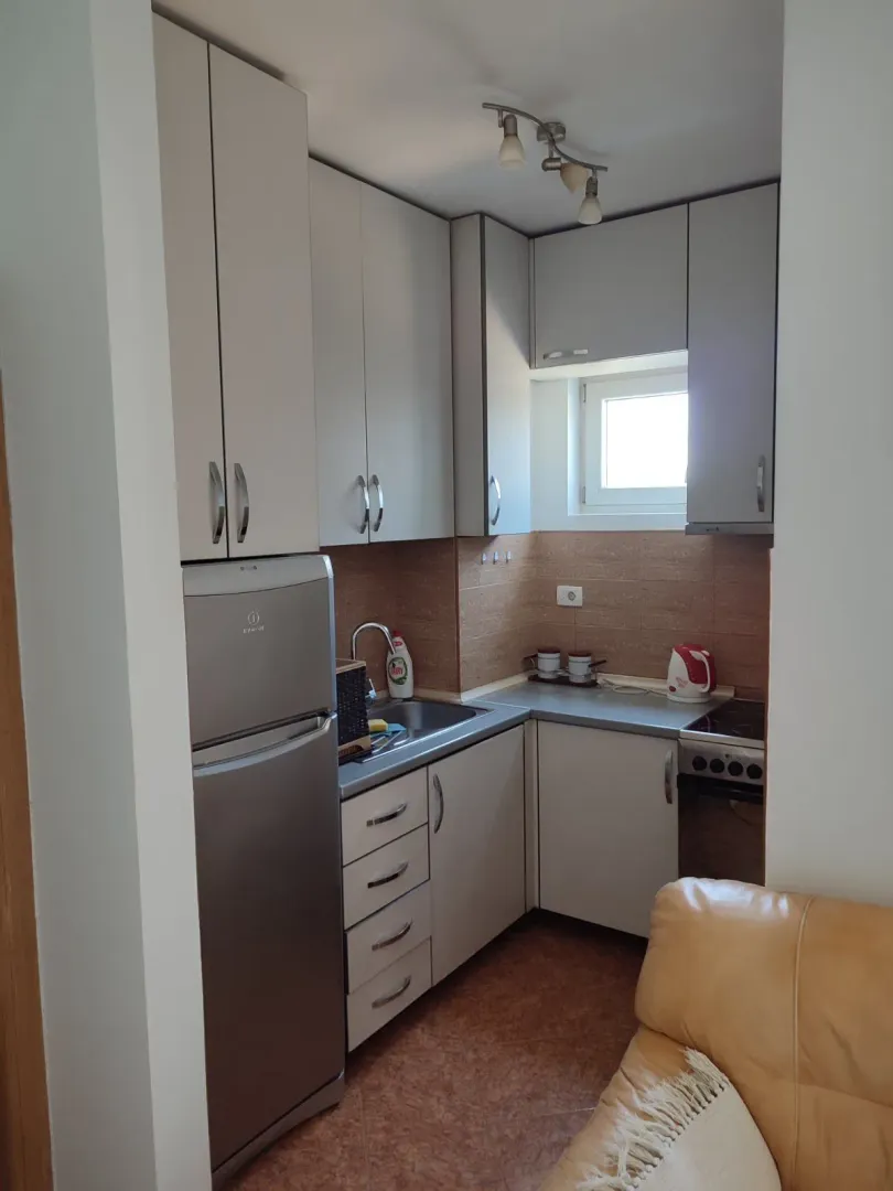 Mala funkcionalna kuhinja sa bijelim elementima i frižiderom.