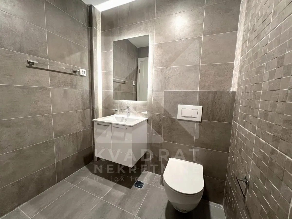 Moderne kupatilo obloženo sivim pločicama sa umivaonikom i wc šoljom.