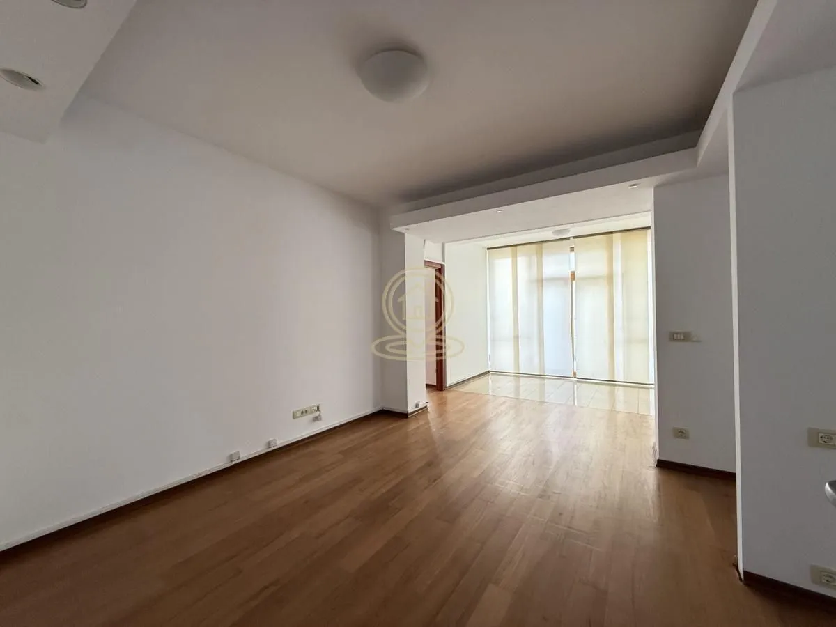 Empty living room with hardwood flooring and a large window.