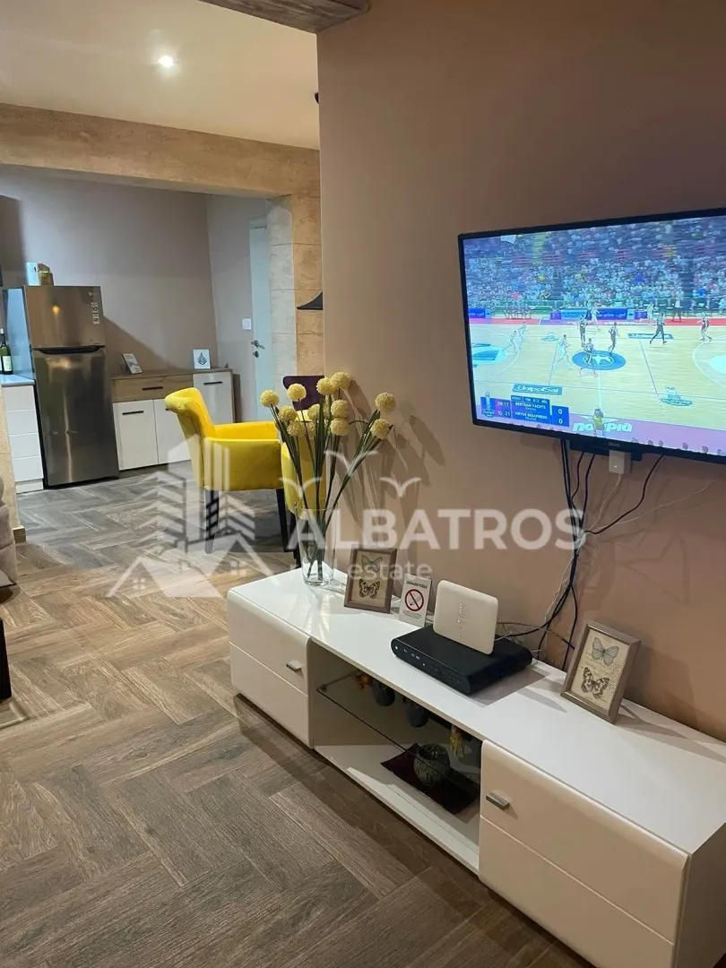Living room with a TV and a view of the kitchen in the background.