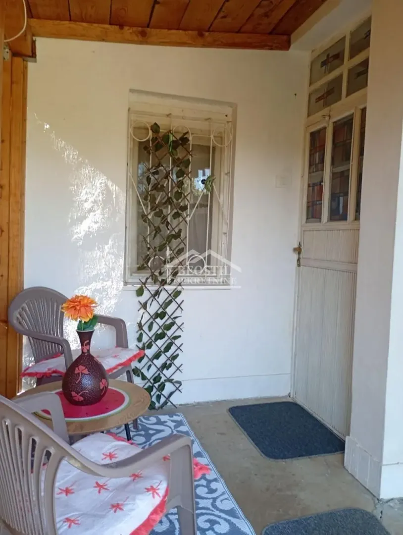 Covered house entrance with seating furniture and decorative plants.