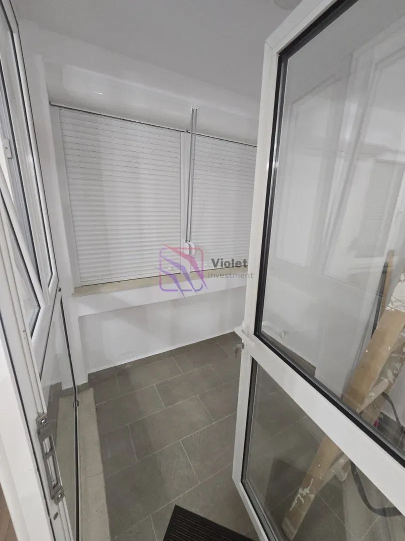 Zastakljeni balkon sa pločicama na podu i bijelim roletnama na prozorima.