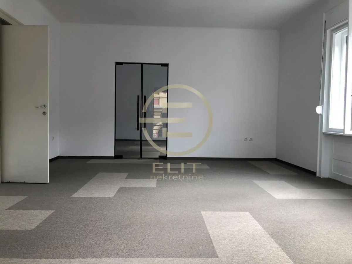 Empty office room with carpet flooring and double glass doors.