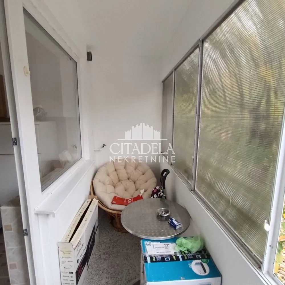 Zastakljeni balkon sa malim stolom i udobnom foteljom.