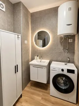 Modern bathroom with a sink, cabinet, water heater, and washing machine. - image 7