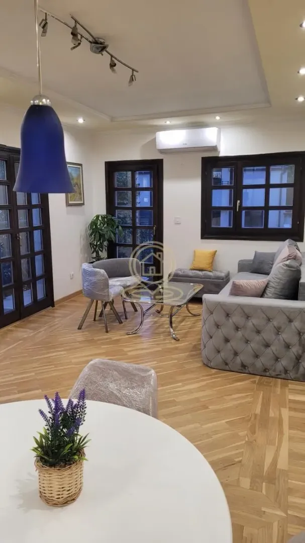 Dnevna soba sa garniturom, foteljom, stočićem i parketom na podu.
