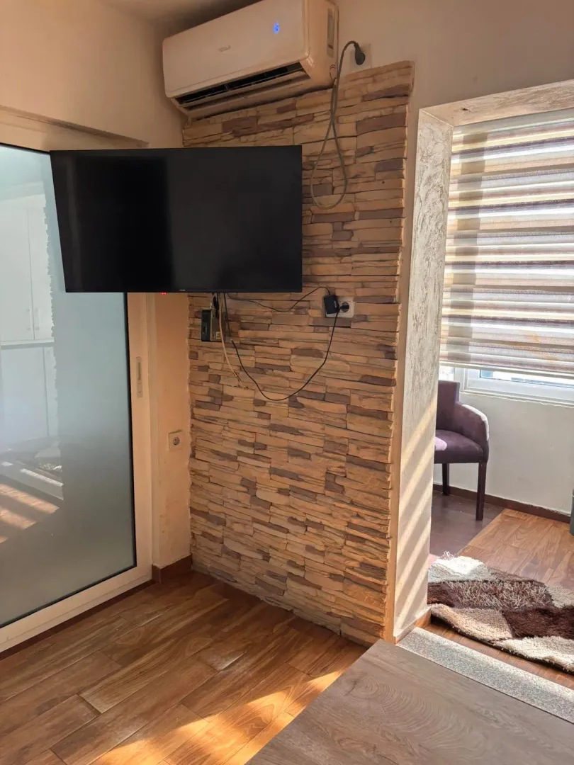Living room with a TV mounted on a decorative stone wall and an air conditioner.