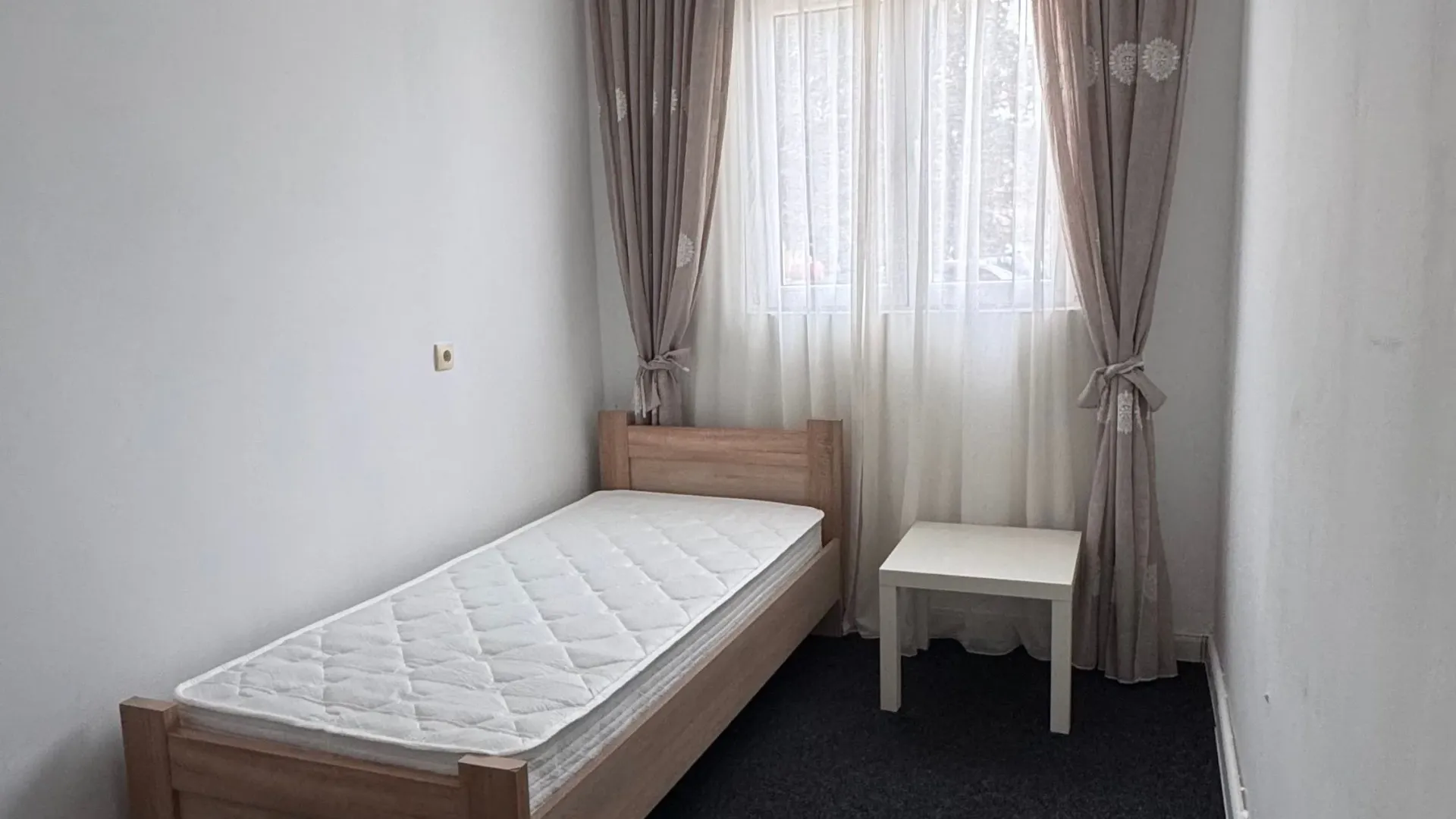 Small bedroom with a wooden bed and a window with curtains.