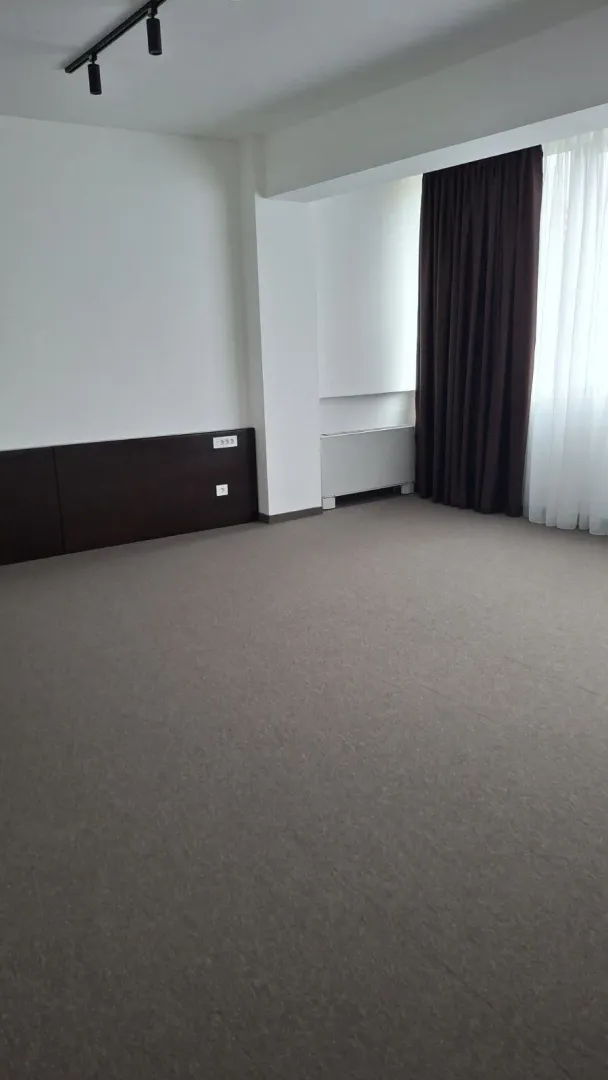 An empty room with grey carpeting and dark curtains.