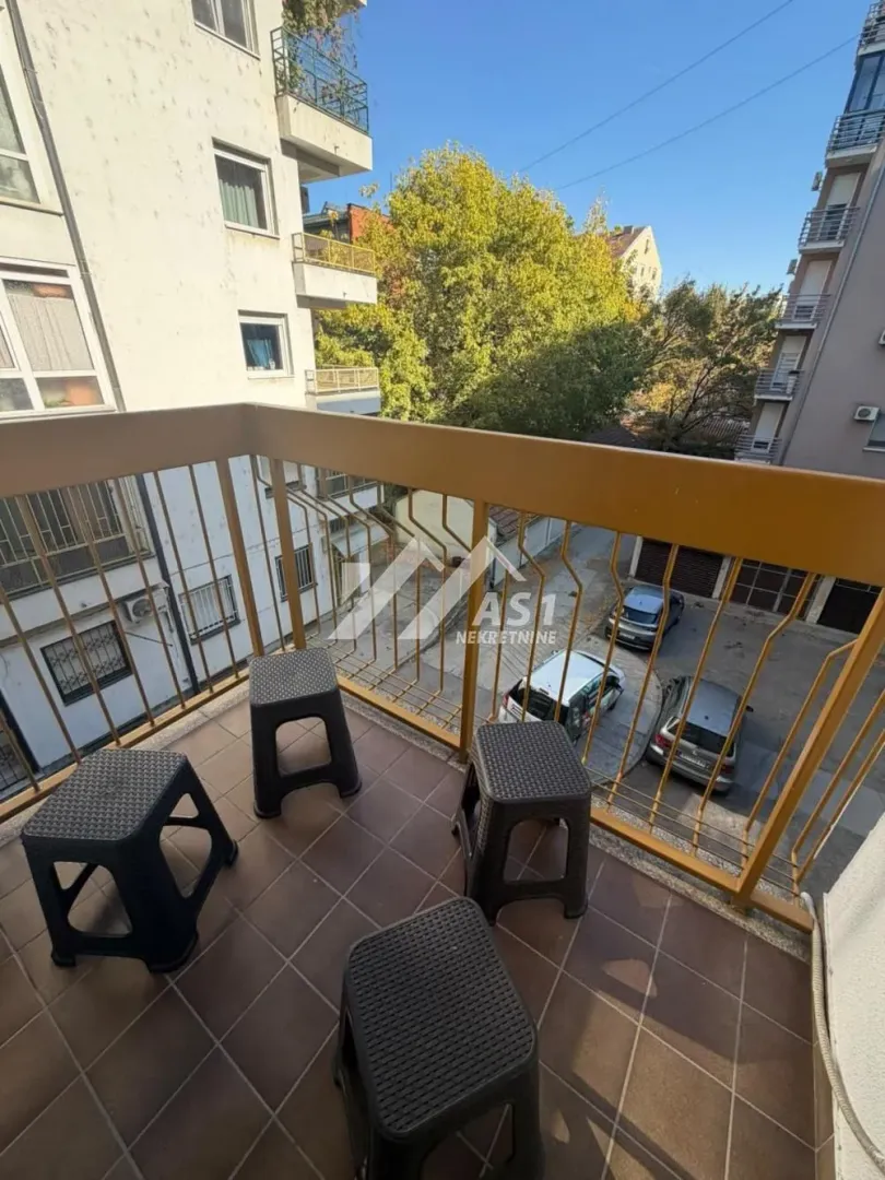Manji popločani balkon sa metalnom ogradom i četiri plastična taburea.