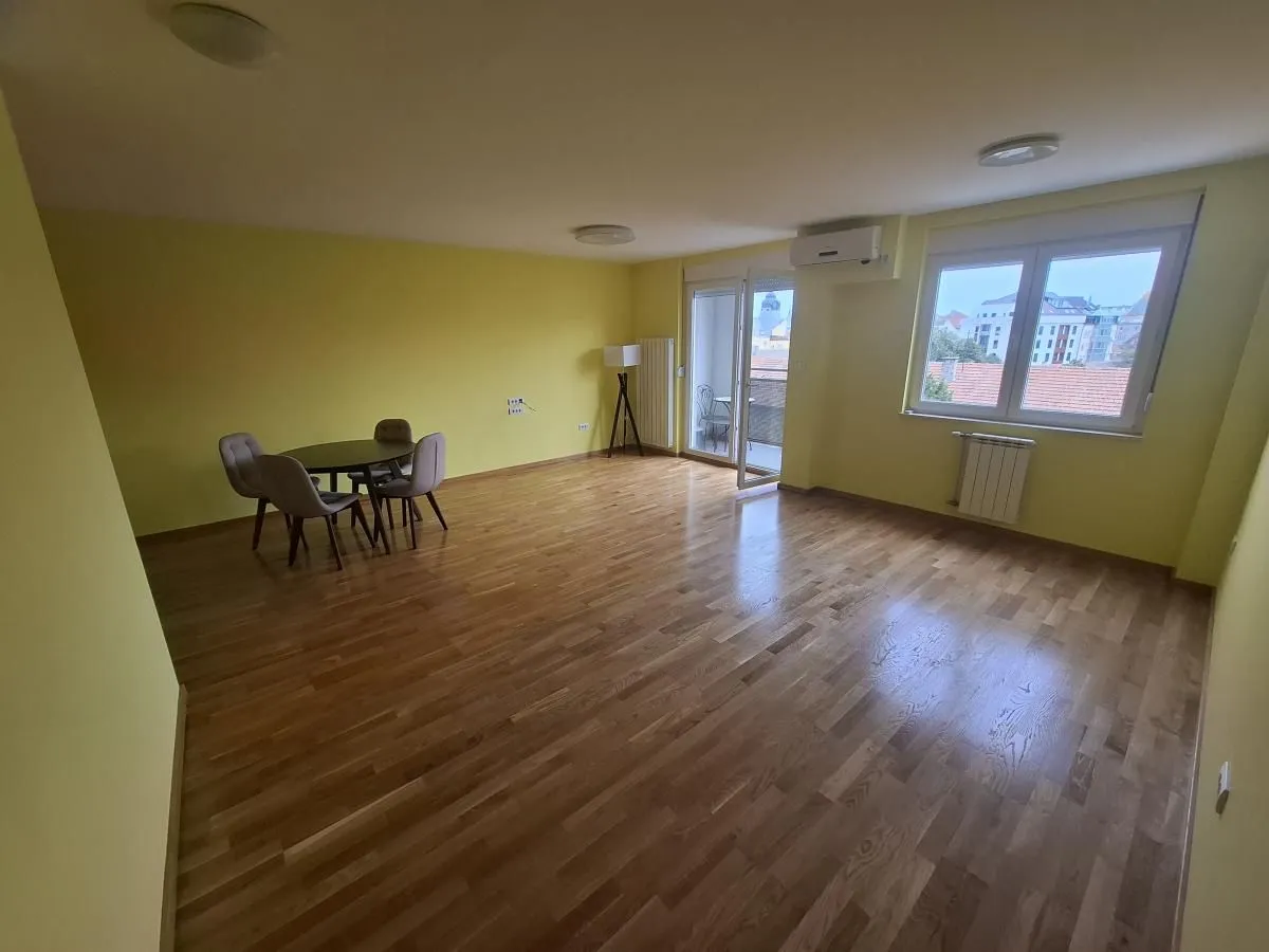 Prostrana dnevna soba sa drvenim podom, trpezarijskim stolom i izlazom na terasu.