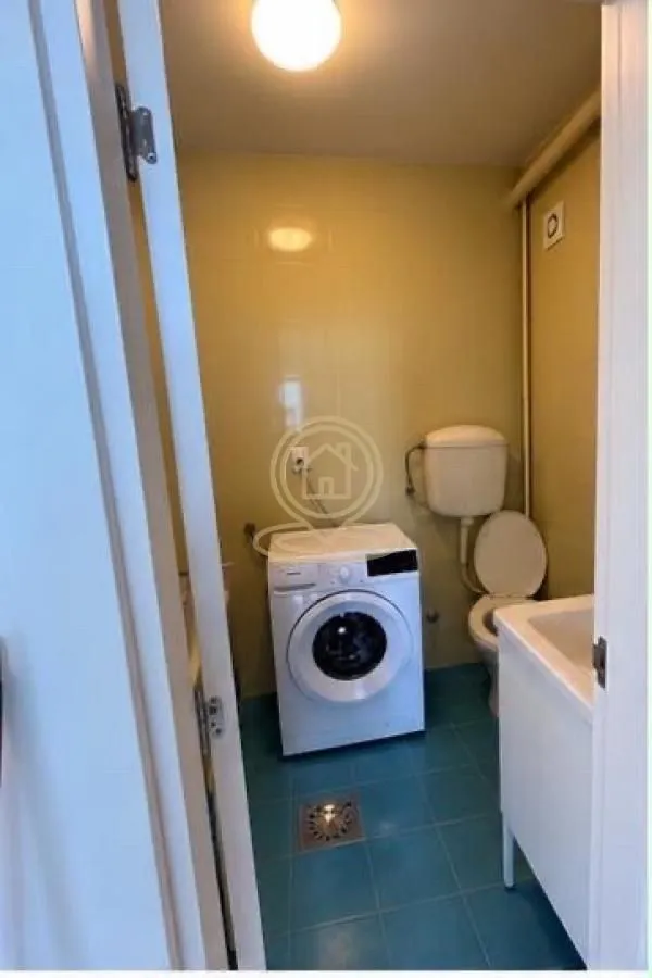 Small bathroom with blue floor tiles, a washing machine, and sanitary fixtures.