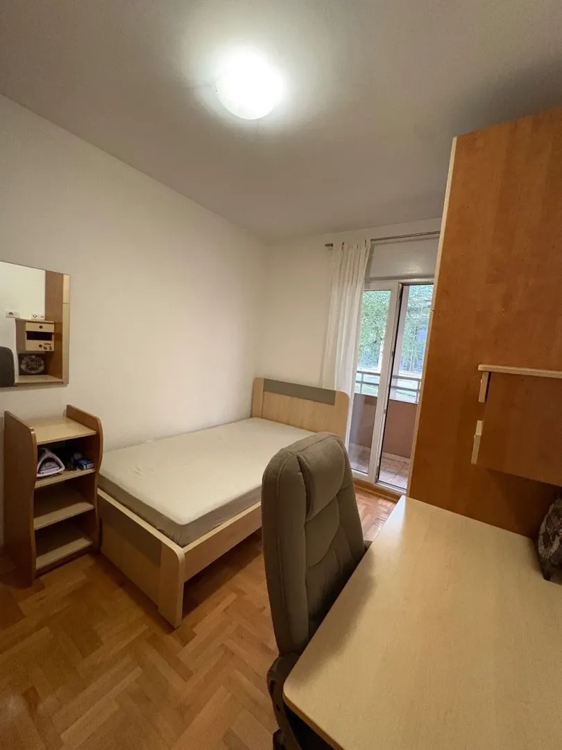 Manja spavaća soba sa krevetom, radnim stolom i izlazom na terasu.