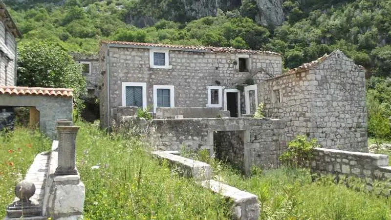 Stara kamena kuća sa dvorištem okružena zelenilom.