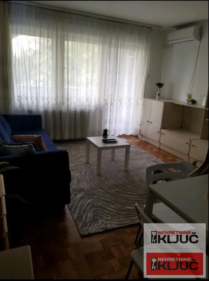 Dnevna soba sa garniturom, stočićem i velikim prozorom.