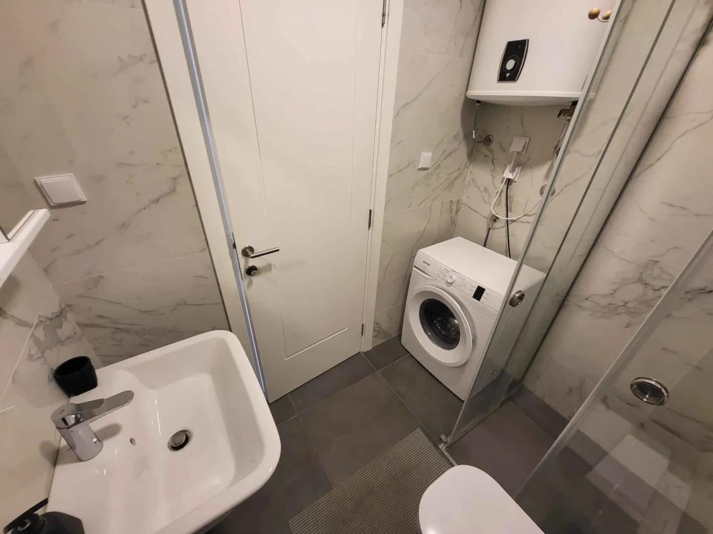 Moderno opremljeno kupatilo sa tuš kabinom i veš mašinom.