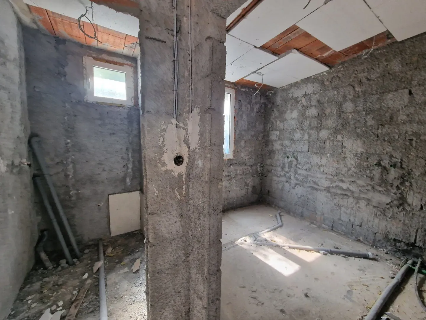 Neuređena prostorija u grubim radovima sa instalacijama i prozorima.