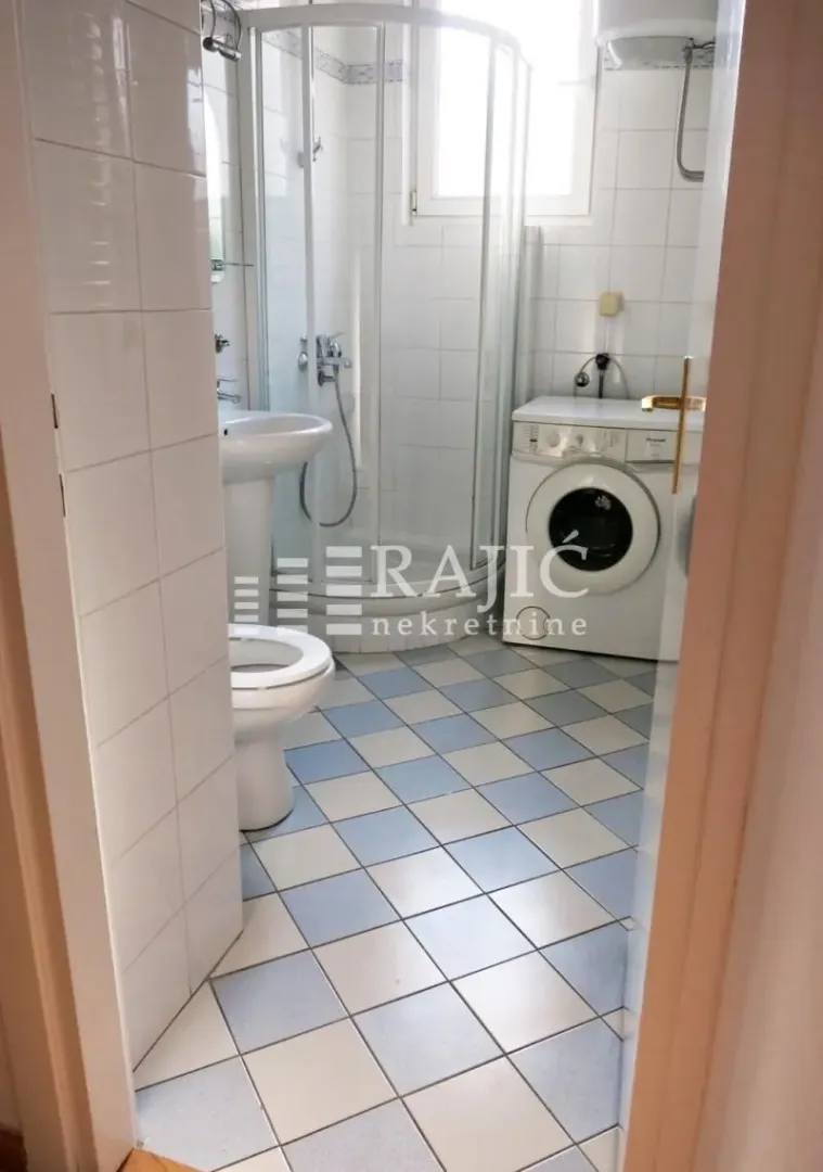 View of the bathroom with a shower cabin, washbasin, and washing machine.