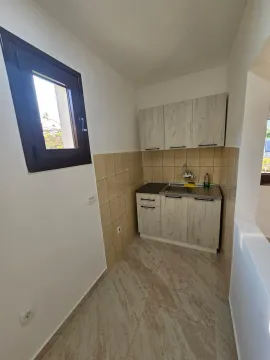 A small kitchen with light wood cabinets and a window. - image 9