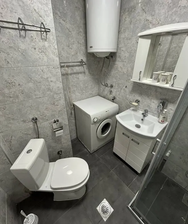 Small bathroom equipped with a shower cabin, sink, toilet, washing machine, and water heater.