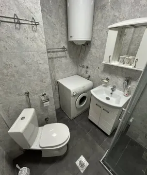 Small bathroom equipped with a shower cabin, sink, toilet, washing machine, and water heater. - image 4