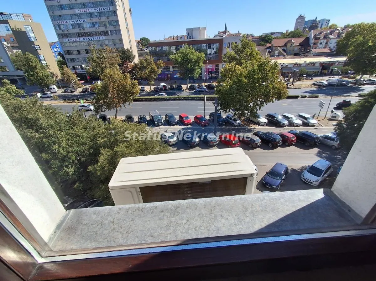 Pogled sa prozora na ulicu, parking i okolne zgrade.
