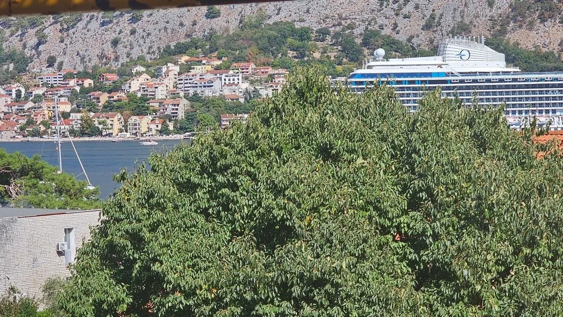 Pogled na zaliv i naselje sa kruzerom u pozadini.