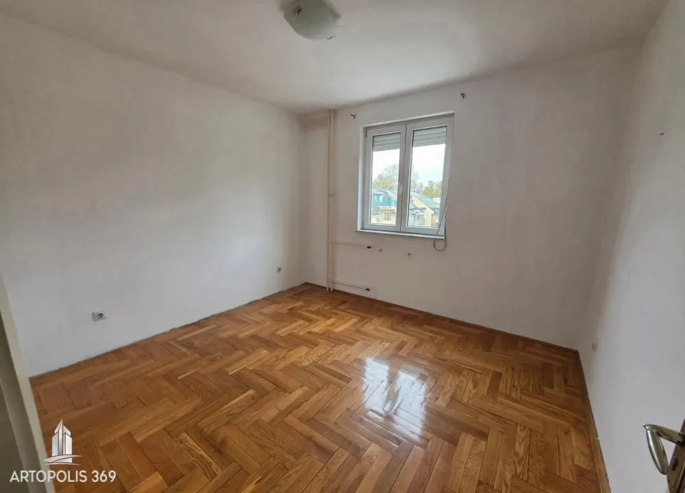 Prazna soba sa parketom i jednim prozorom.