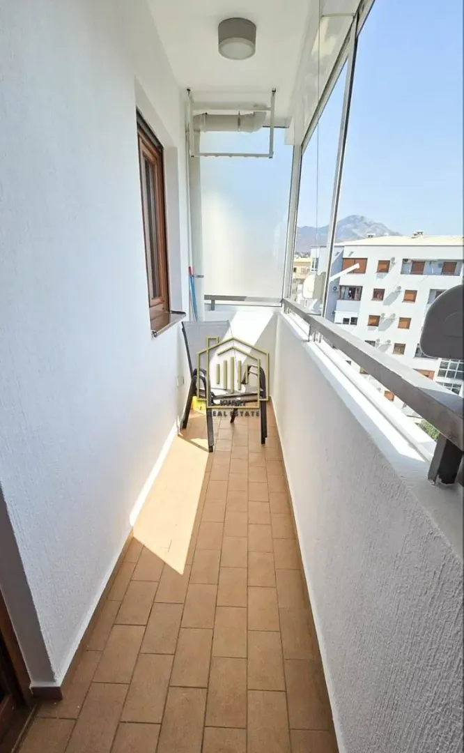 Dugačak zastakljeni balkon sa keramičkim pločicama i stolicom.